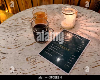 Drei Gläser Glühweinpunsch auf einem rustikalen Holztisch mit einer Speisekarte mit Getränkeoptionen und Preisen, beleuchtet von einer Kerze in einer gemütlichen Atmosphäre Stockfoto