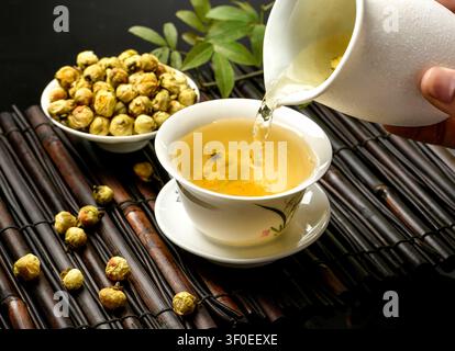 Heißer Chrysanthementee wird in eine weiße Keramik Tasse auf einer Bambusmatte gegossen Stockfoto