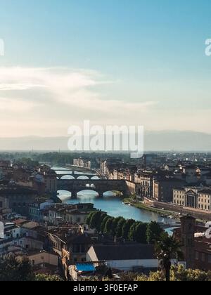 Blick auf die historische Ponte-Vecchio-Brücke, die den Arno überquert, mit umgebenden Steingebäuden und üppigen Bäumen in Florenz, Toskana, Italien. Stockfoto