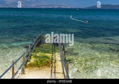 Eine Beton-Zufahrtsrampe mit Metallgeländern, die direkt ins Adriatische Meer führt und sicheren und bequemen Zugang für Rollstuhlfahrer und Menschen bietet Stockfoto