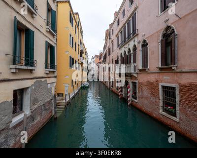 Ein malerischer Blick entlang eines schmalen Wasserkanals, gesäumt von historischen, farbenfrohen venezianischen Gebäuden, Fensterläden und Anlegestellen unter einem ove Stockfoto