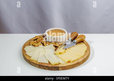 Sogar dreieckige Käuse werden auf einem Holzbrett geschnitten. Daneben liegen eine Handvoll Walnüsse und eine kleine Schüssel Honig. All dies wird ergänzt Stockfoto