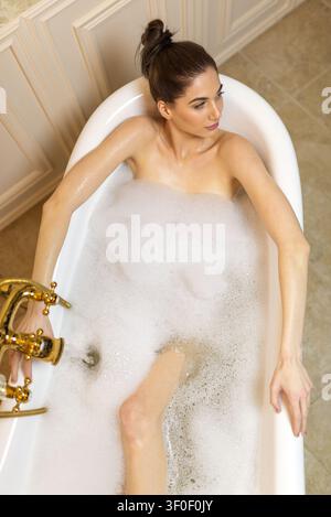 Schöne Frau entspannt sich in einer vollen Badewanne mit ausgebreiteten Armen Stockfoto