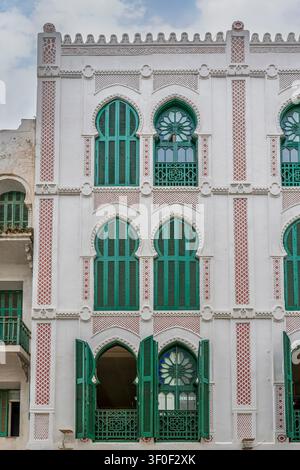 Ein mehrstöckiges Gebäude im spanischen Kolonialviertel von Tetouan zeigt eine verzierte weiße Fassade mit wiederholten rot gekachelten Pilastern, spitzbogigen Gothi Stockfoto