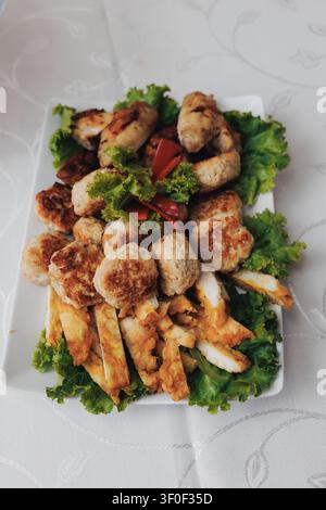 Goldbraune Fleischbällchen liegen in knusprigem Salat. Frische Tomaten verleihen dem Gericht Farbe und Kontrast. Gebratene Calamares-Spiralen umgeben die Hauptattraktion. Stockfoto