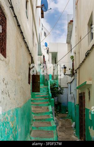Eine schmale, stufenartige Gasse in der UNESCO-geschützten Medina von Tetouan zeigt Wände, die in verblassten Grün- und Minttönen gestrichen sind, wobei der Putz abblättert und altes Mauerwerk freilegt Stockfoto