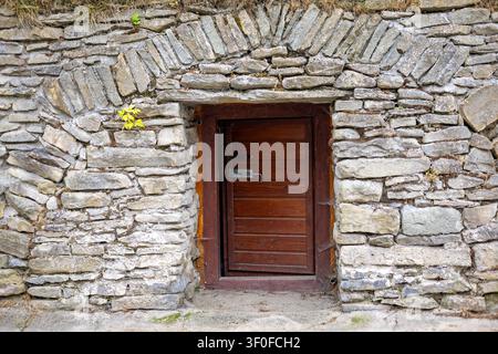 Verwitterte Holztür in rustikaler Steinmauer. Verwitterte Holztür in einer rustikalen Steinmauer mit gewölbtem Mauerwerk, Metallriegel, rau Stockfoto