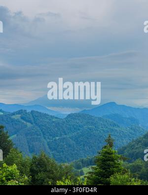Nebliges Berglandschaft mit geschichteten bewaldeten Hügeln unter dramatischen Wolken Stockfoto