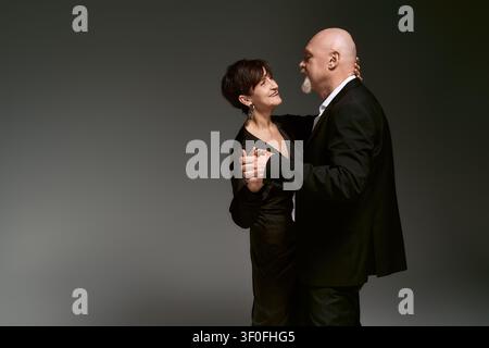 Ein liebevolles Seniorenpaar teilt einen fröhlichen Tanz und zeigt dabei ihre tiefe Bindung, während sie elegant gekleidet sind. Stockfoto