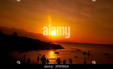 Ein leuchtender Sonnenuntergang erfüllt den Himmel über einer ruhigen tropischen Küste mit ruhigem Meer und warmen Reflexionen, perfekt für Reise- und Naturkonzepte. Stockfoto