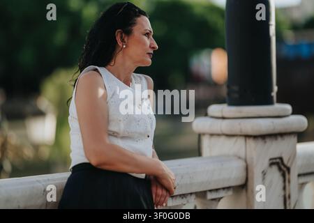 Frau, die sich auf ein Marmorbrückengeländer lehnt und in einem Sommerporträt im Freien nachdenklich aussieht Stockfoto