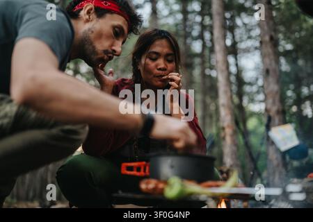 Paar kocht über einem Lagerfeuer, während es zusammen im Wald im Freien campiert Stockfoto