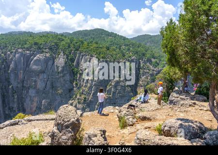 Besucher stehen auf felsigen Klippen mit Blick auf das Tazi-Canyon in den Taurus-Bergen, Antalya, umgeben von üppigen Bäumen und einem klaren blauen Himmel Stockfoto