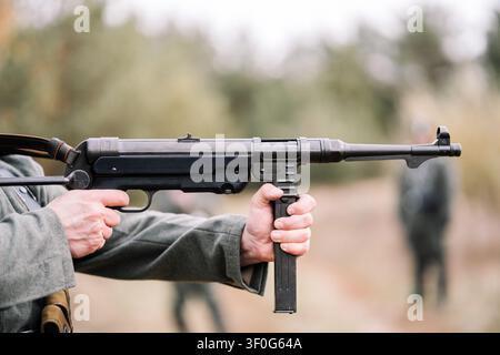 Nahaufnahme von Händen, die eine MP-40-Maschinenpistole abfeuern, während einer historischen Nachstellung. Thema Kriegsexekution, NS-Verbrechen und Völkermord im Zweiten Weltkrieg. Stockfoto