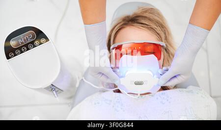 Isolierte Aufnahme einer Patientin beim Zahnarzt in der Praxis. Zahnaufhellungsverfahren mit Ultraviolett-Licht-UV-Lampe. Professioneller Zahnarzt verwendet spezielle Ausrüstung für das Verfahren. Stockfoto