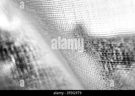 Das Bild ist eine Nahaufnahme, eine Schwarz-Weiß-Ansicht eines texturierten Stoffes. Der Stoff weist ein sichtbares Gewebemuster auf, mit dunkleren Flecken und Linien, die darauf erscheinen Stockfoto