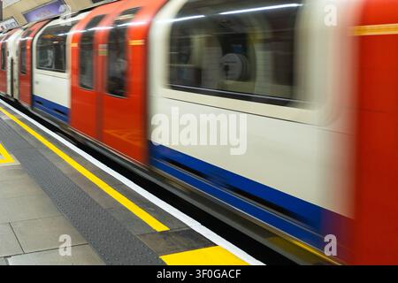 U-Bahn-Zug der London Underground, der mit Bewegungsunschärfe an einem Bahnsteig vorbeirast Stockfoto