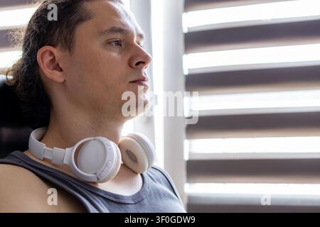 Porträt eines konzentrierten Mannes mittleren Alters mit weißen kabellosen Over-Ear-Kopfhörern, die um seinen Hals liegen, während er während der Arbeit zu Hause nachdenkt. Konzept von Stockfoto
