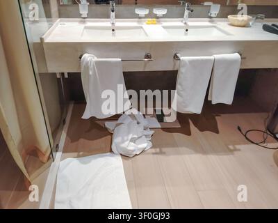 Badezimmerinnenraum mit einem modernen Doppelsink, an dem weiße Handtücher auf einem Handtuchhalter hängen, und einer Badematte auf dem Boden, der ein sauberes und Stockfoto