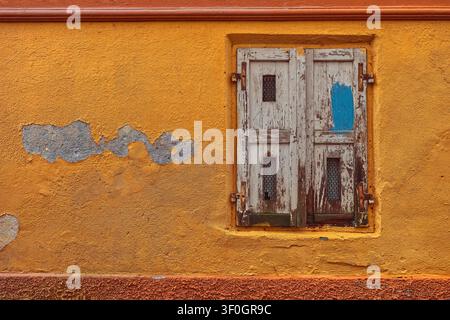 144 Erdgeschossfenster mit verfallenen weißen Holzläden an der abgeblätterten orangefarbenen Fassade eines Hauses in der Klobovsova ulica. Skofja Loka-Slowenien. Stockfoto