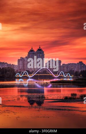 Wunderschöner Sonnenuntergang über der Obolon-Terrasse in Kiew, Ukraine, ruhige Spiegelungen auf dem Wasser und ein leuchtendes Stadtbild im warmen Abendlicht. Stockfoto
