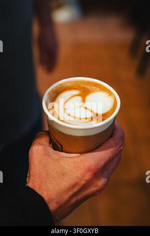 Hohe Blickwinkelansicht einer Person, die eine Tasse Latte mit Kunst hält Stockfoto