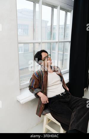 Ein junger, gutaussehender Asiate in eleganter Kleidung sitzt lässig und genießt den ruhigen Blick. Stockfoto