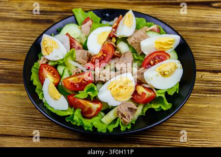 Leckerer Thunfischsalat mit Eiern, Salat und frischem Gemüse auf Holztisch Stockfoto