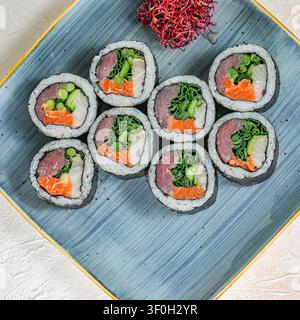 Eine farbenfrohe Auswahl an Sushi-Rollen und geschnittenem Gemüse, wunderschön auf einem blauen Teller arrangiert. Stockfoto