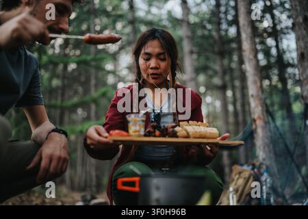 Freunde kochen und teilen Essen beim Campen in einem Wald über einem kleinen Lagerfeuer Stockfoto