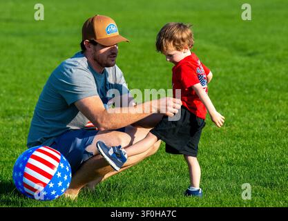 Ein Vater gibt seinem Sohn eine helfende Hand, während sie im Stadtpark von Montrose, Colorado, Fußball spielen. Stockfoto
