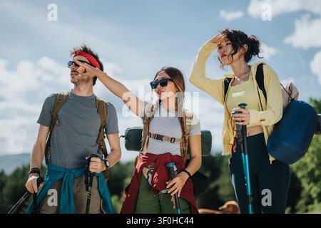 Drei Freunde wandern mit Rucksäcken und Trekkingstöcken auf einem sonnigen Bergpfad Stockfoto