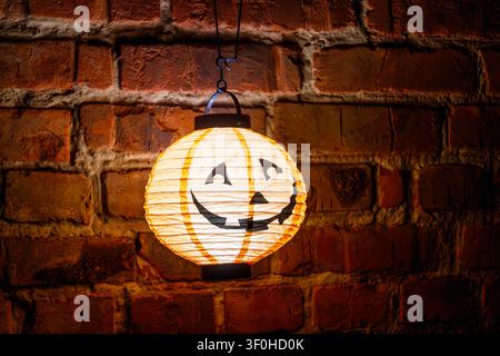 Lächelnder leuchtender Kürbislaterne, die nachts an einer alten roten Backsteinmauer hängt. Halloween-Dekorationskonzept Stockfoto