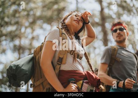 Junge Wanderer mit Rucksäcken, die während einer Sommertour gemeinsam in einem sonnenbeschienenen Wald eine Pause einlegen Stockfoto