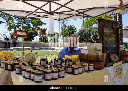 Ein italienischer Imker verkauft Biohonig und Bienenprodukte unter einem Zeltdach auf einem lokalen Straßenmarkt in Civitavecchia, Lazio, Italien. Stockfoto
