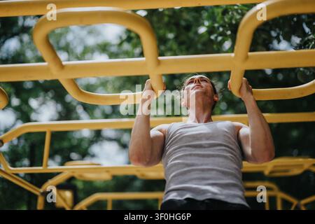Junger Mann führt Klimmzüge an gelben Affenstäben in einem Outdoor-Fitnesspark während des Trainings durch Stockfoto