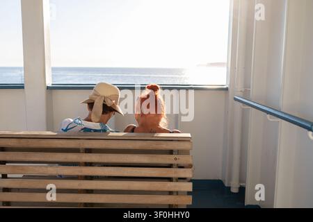 Passagiere sitzen auf Holzbank auf dem Deck eines Fährboots und blicken auf das Meer in Malta, 19. Juni 2026. Stockfoto
