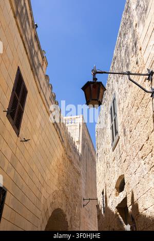 Schmale alte Straße mit alten Kalksteinmauern und antiker Laterne vor blauem Himmel. Stockfoto