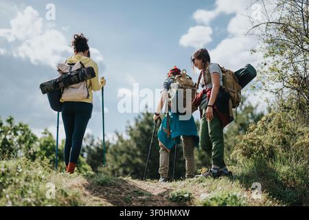 Drei Freunde wandern auf einem Waldweg mit Rucksäcken und Trekkingstöcken an einem sonnigen Tag Stockfoto