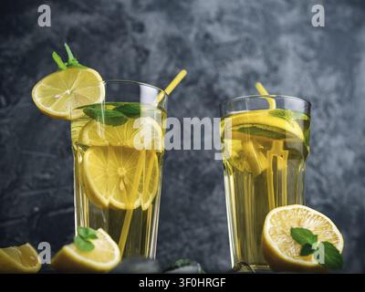 Traditioneller geeister Zitronen- und Minze-Eistee. Mojito in zwei Gläsern auf einem dunklen Betonstisch Stockfoto