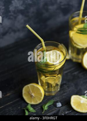 Traditioneller geeister Zitronen- und Minze-Eistee. Mojito in zwei Gläsern auf einem dunklen Betonstisch Stockfoto