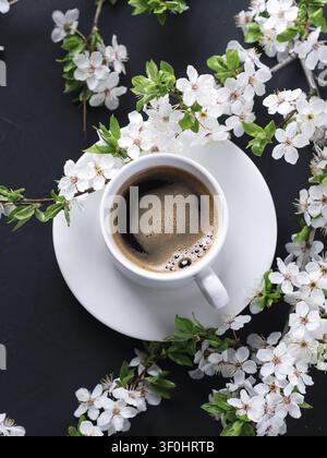 Eine Tasse duftender frisch gebrühter Kaffee und blühende Zweige von Frühlingskirschen Stockfoto
