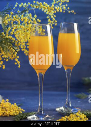 Mimosa-Cocktail und gelbe Mimosenblüten auf einem blauen Tisch. Alkoholarmer Cocktail mit Sekt und Orangensaft Stockfoto