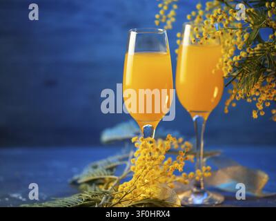 Mimosa-Cocktail mit Blumen auf blauem Hintergrund Stockfoto