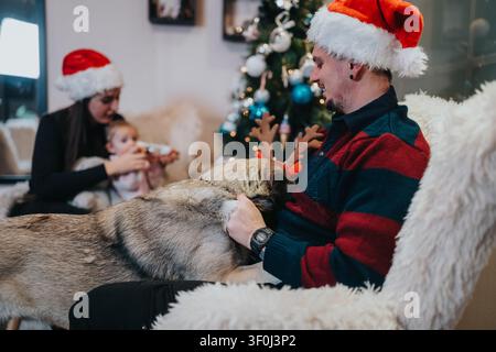 Familie versammelt sich am Weihnachtbaum mit einem Hund auf dem Schoß in einem gemütlichen Feiertags-Wohnzimmer Stockfoto