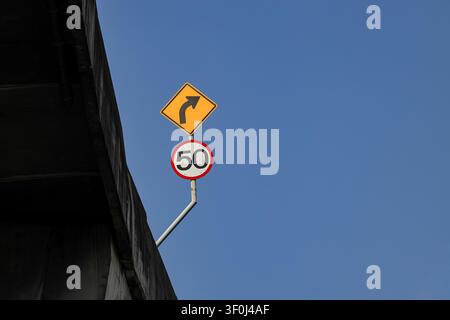 Verkehrsschilder zeigen eine Geschwindigkeitsbegrenzung von 50 Kilometern pro Stunde auf den Straßen und ein Warnschild für die rechte Kurve am Rand der Hochstraße. Stockfoto