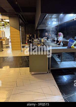 Konakli, Alanya - 20. Mai - Frauenköche mit Kopftüchern bereiten warme Mahlzeiten in einer modernen Gewerbeküche zu. Offener Buffet-Tresen mit aufsteigendem Dampf aus Stockfoto