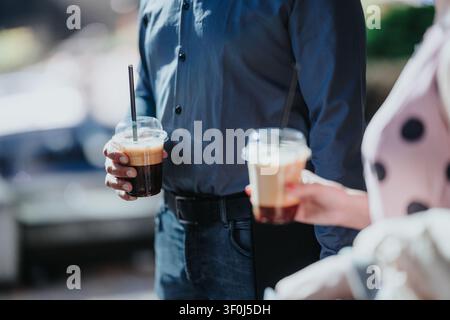 Paar hält Eiskaffee-Drinks im Freien, während es zusammen in lässiger Kleidung steht Stockfoto