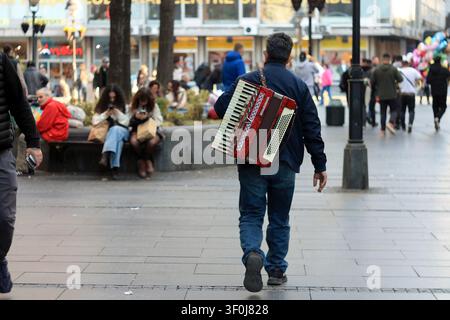 Lokaler Musiker trägt ein rotes Akkordeon und geht durch die Knez-Mihailova-Straße in Belgrad (Serbien) Stockfoto