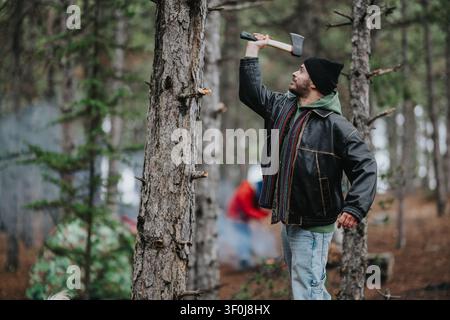 Freunde campen in einem Bergwald, während ein Mann sich bereitmacht, mit einer Axt Holz zu spalten Stockfoto